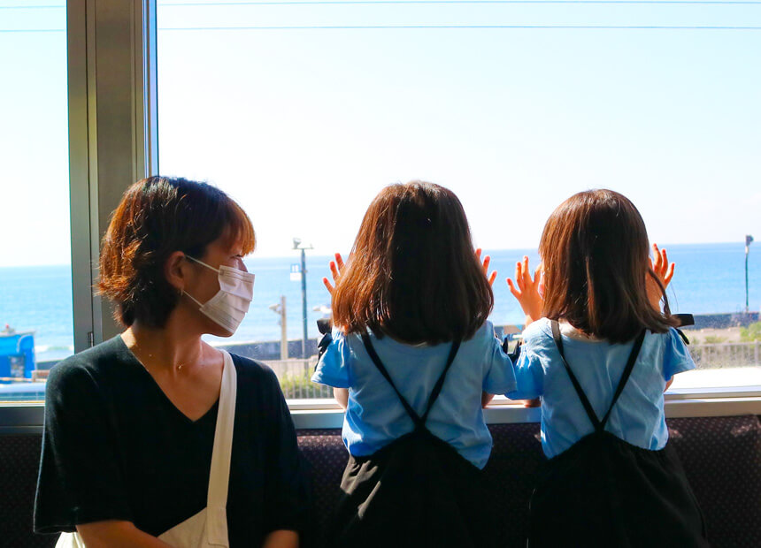 江ノ電車内から鎌倉の海を眺める子どもたち