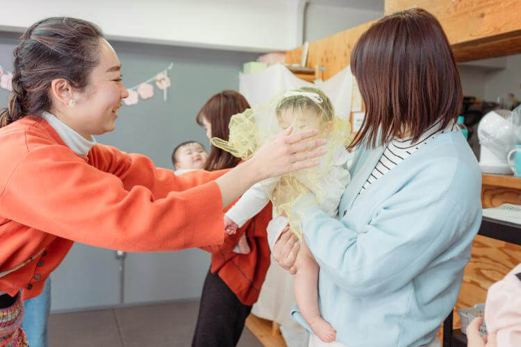 ママに抱っこされる赤ちゃんに触れ合う先生